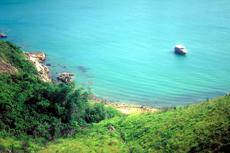 hill slope and blue sea lagoon with small boat seen from hilltop