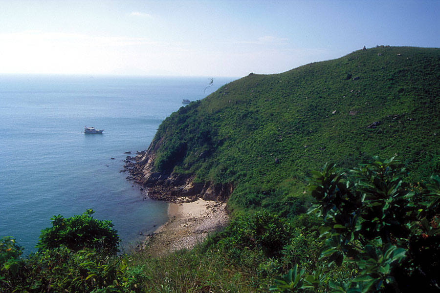 hill side and pale blue sea with small boat and white sky horizon