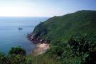 hill side and pale blue sea with small boat and white sky horizon