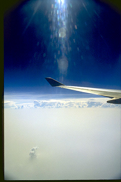 deep blue sky above the clouds with airplane wing; sun ray scatter through plane window