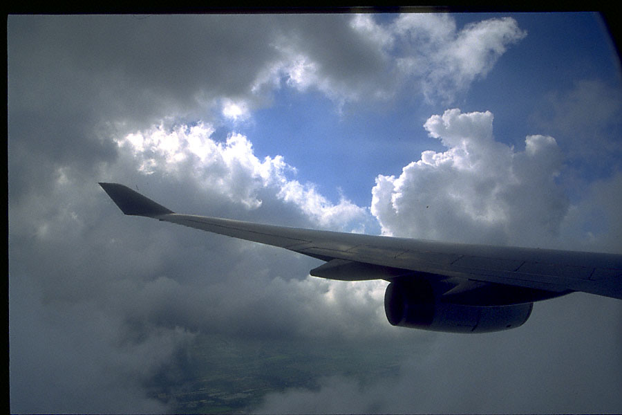 plane wing passing through cumulus cloud; white/blue sky