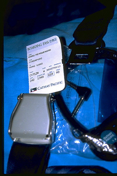 captioned image of plane ticket stub seen with seat belt buckle and headphones in seat