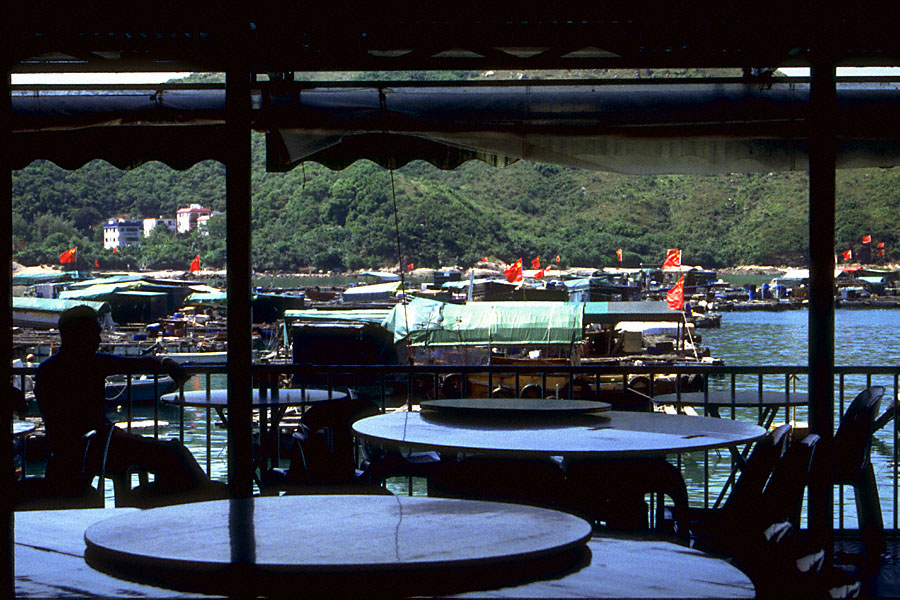 restaurant silhouette with tables and awning with boats, flag, and green hill