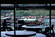 restaurant silhouette with tables and awning with boats, flag, and green hill